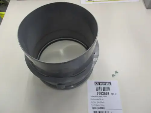 Grauer Adapter von Remeha mit einem Anschlussstück. Im Bild sind auch Schrauben zu sehen. Das Produkt hat eine runde Öffnung und eine flache Unterseite.